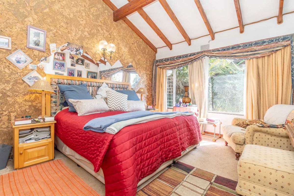 Spacious bedroom featuring exposed timber ceiling beams, unique cork wall paneling, and large windows providing natural light and garden views.