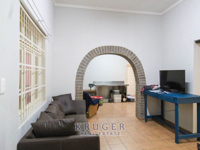 A living area featuring tiled flooring and a distinctive brick archway leading to an adjacent space, with security bars fitted to the window.