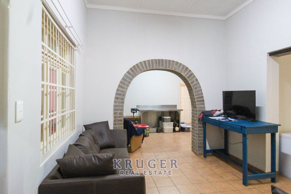 A living area featuring tiled flooring and a distinctive brick archway leading to an adjacent space, with security bars fitted to the window.