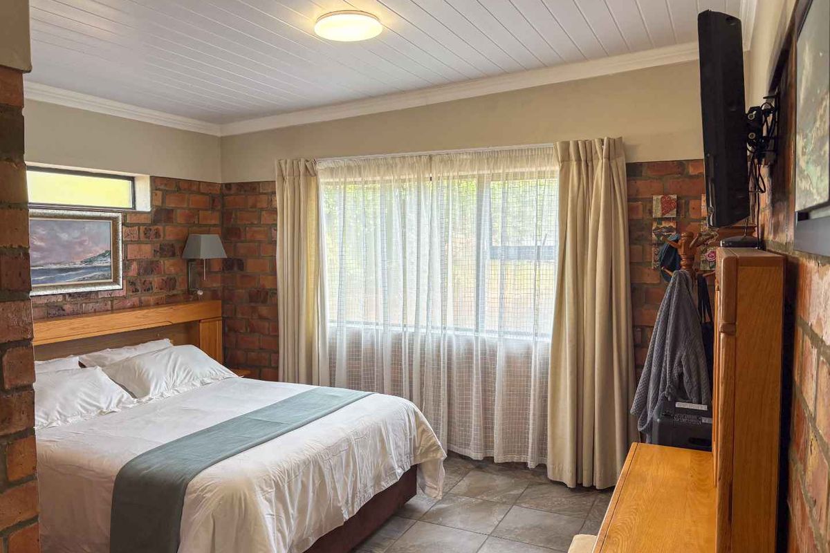 A bedroom featuring exposed brick walls, tiled flooring, and a white tongue-and-groove ceiling, providing a rustic and textured aesthetic.