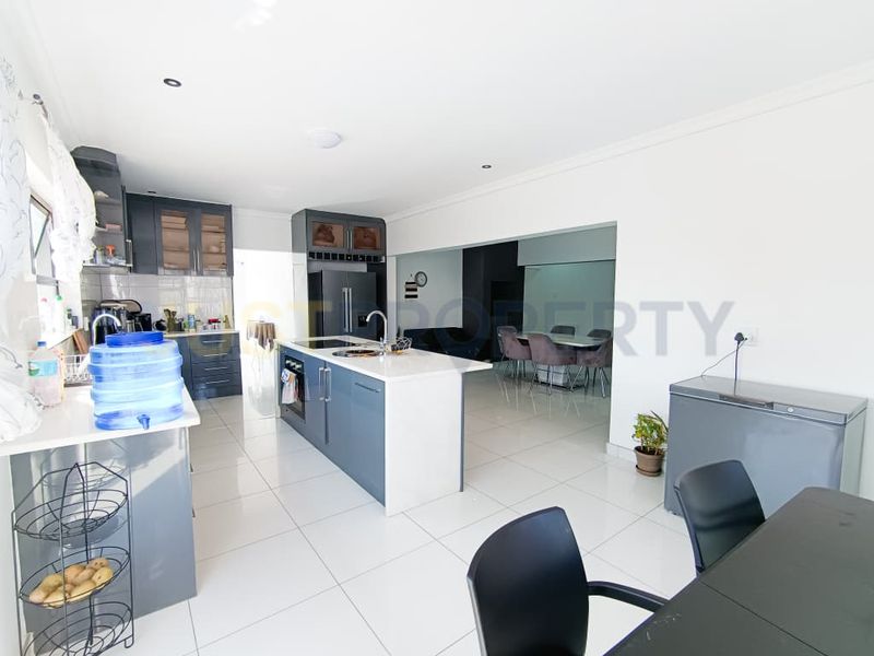 Modern open-plan kitchen featuring a central island, sleek dark cabinetry, and light tiled flooring, seamlessly flowing into the adjacent dining area.