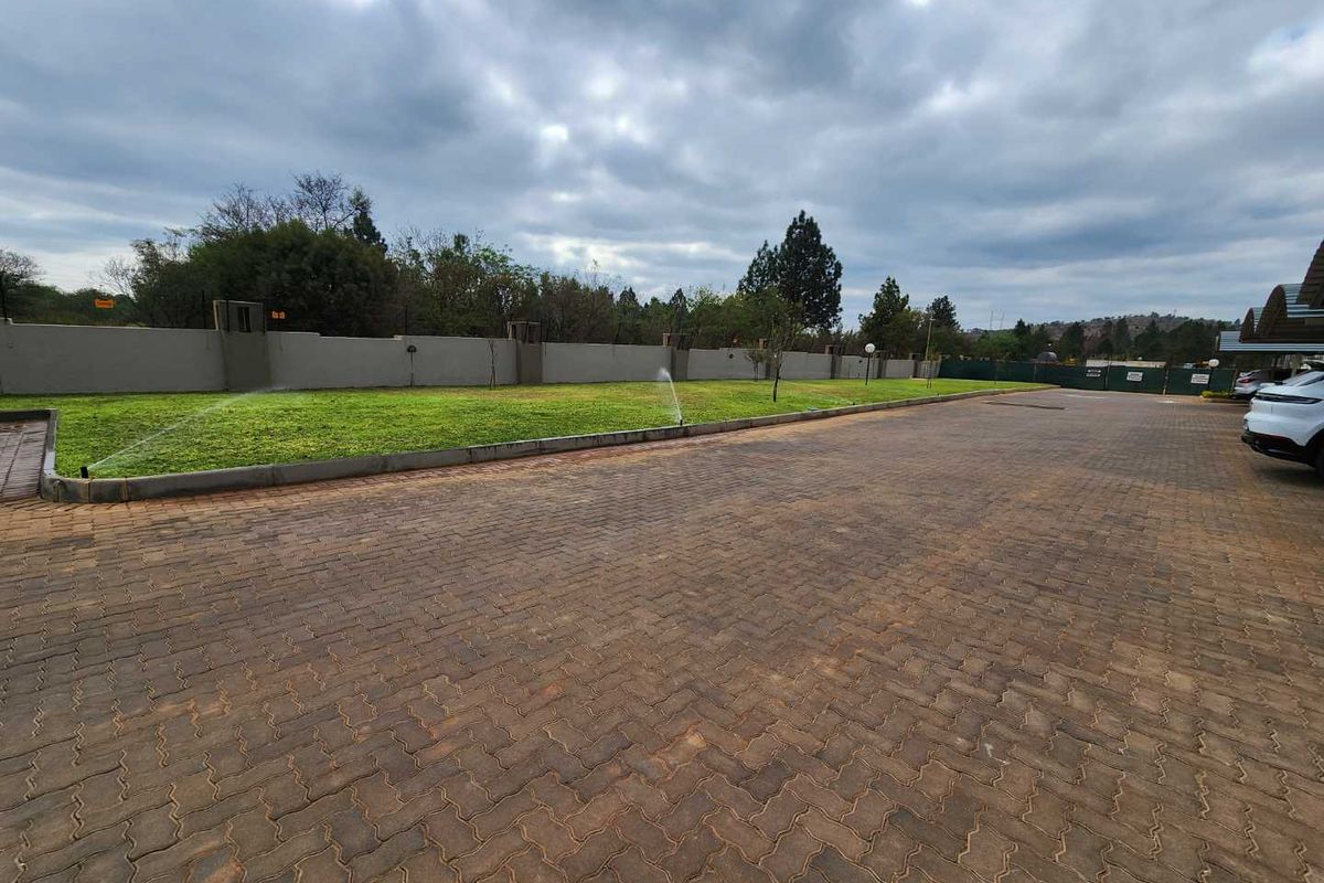 A well-maintained paved driveway area featuring a perimeter wall, manicured lawn, and an active sprinkler system.