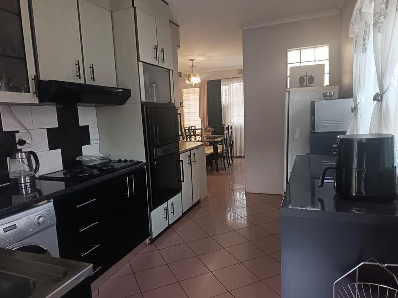 A functional kitchen featuring built-in cabinetry, a hob, an extractor fan, and a built-in oven, with tiled flooring and a view into the dining area.