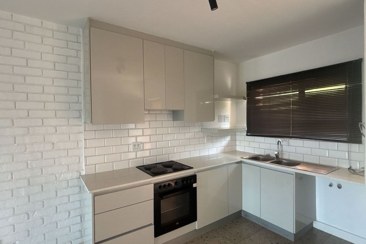Modern kitchen featuring sleek cabinetry, subway tile backsplash, built-in oven and hob, and a double sink with a window view.