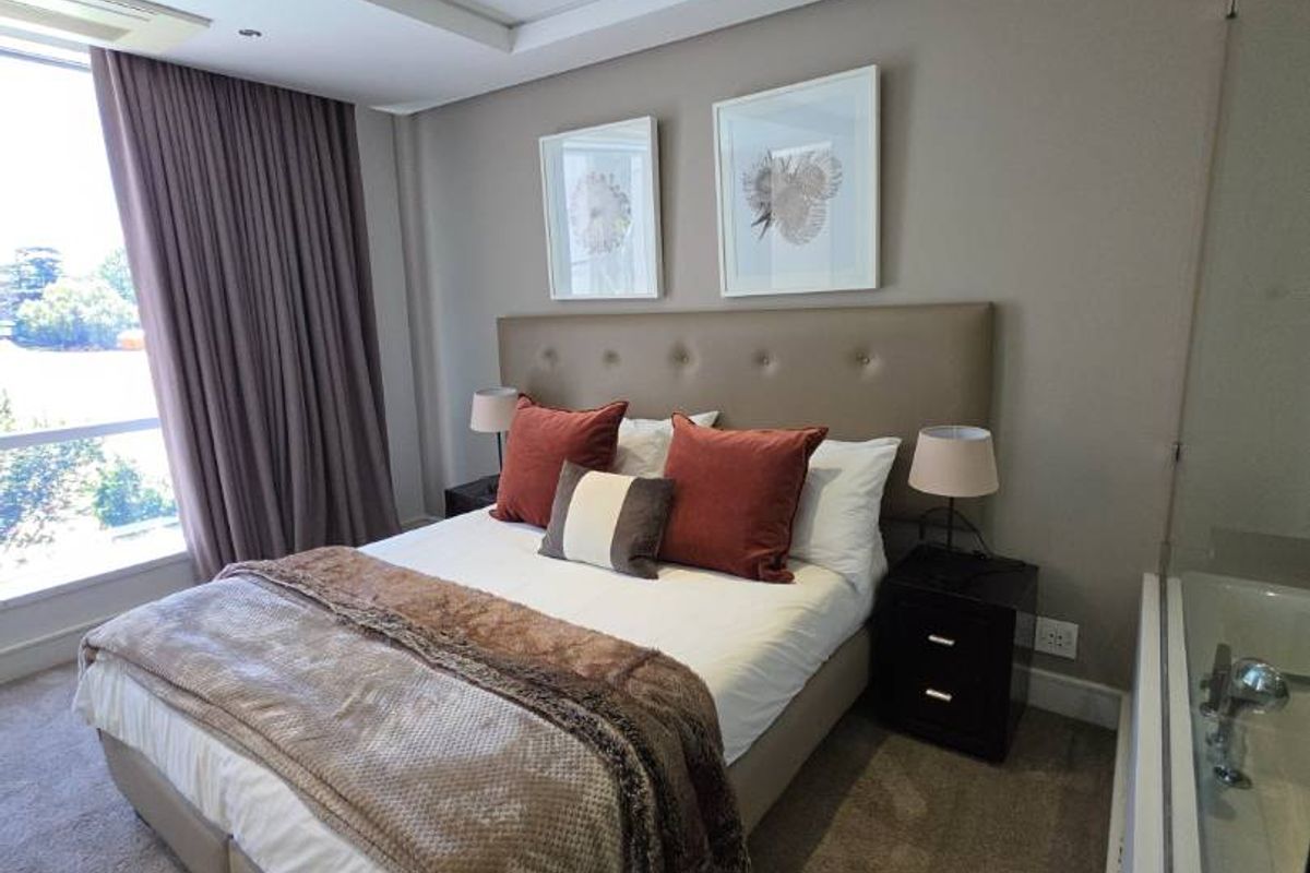 A well-appointed bedroom featuring plush carpeting, recessed ceiling lighting, and large windows with floor-to-ceiling curtains, offering a comfortable and modern living space.