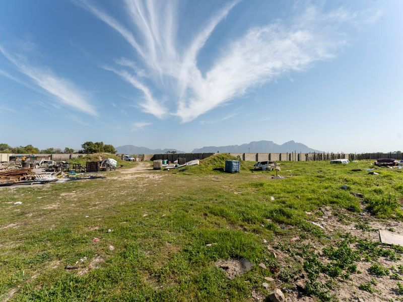 A large vacant residential plot featuring a perimeter boundary wall and mountain views, currently requiring significant site clearance and debris removal.