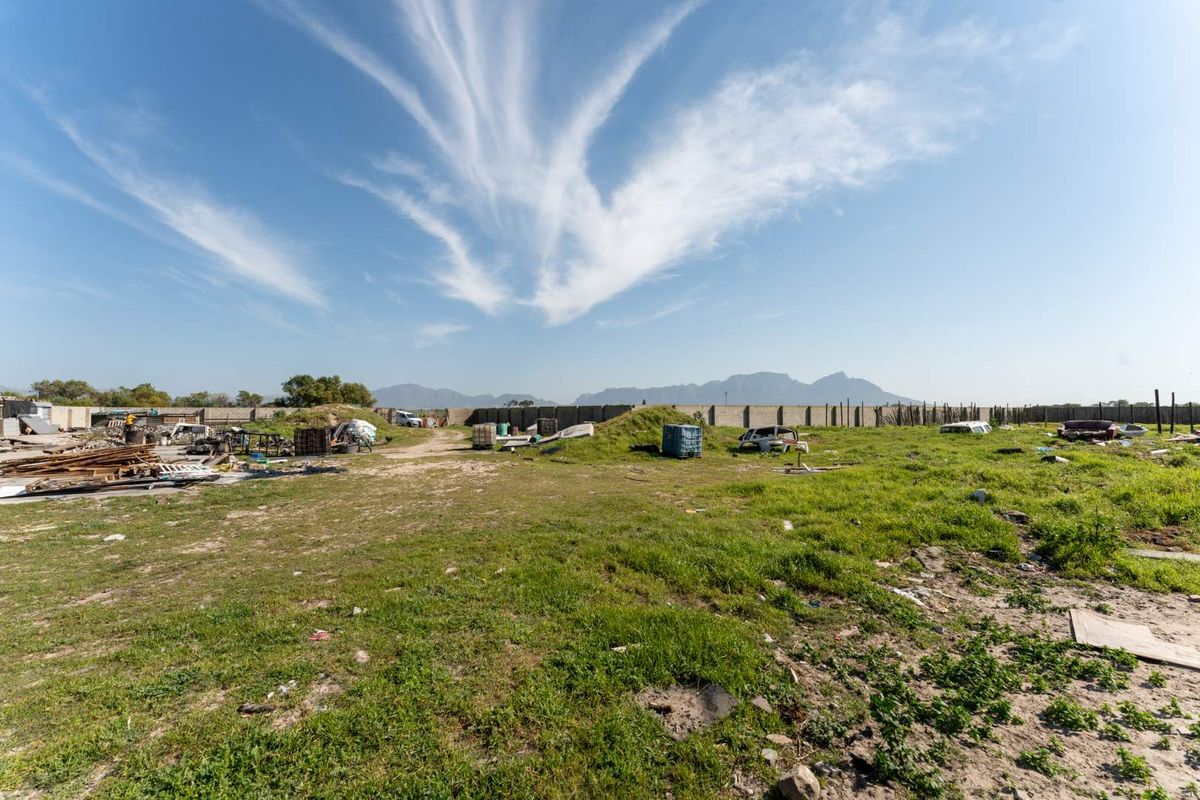A large vacant residential plot featuring a perimeter boundary wall and mountain views, currently requiring significant site clearance and debris removal.