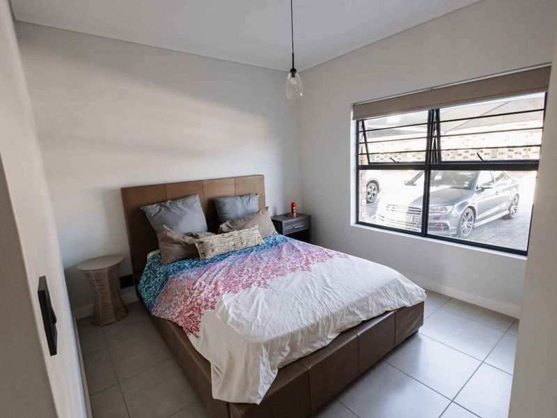 A well-maintained bedroom featuring neutral tiled flooring, a large window with security bars, and a modern pendant light fixture.