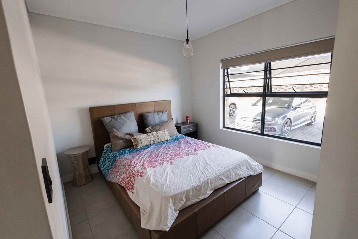 A well-maintained bedroom featuring neutral tiled flooring, a large window with security bars, and a modern pendant light fixture.