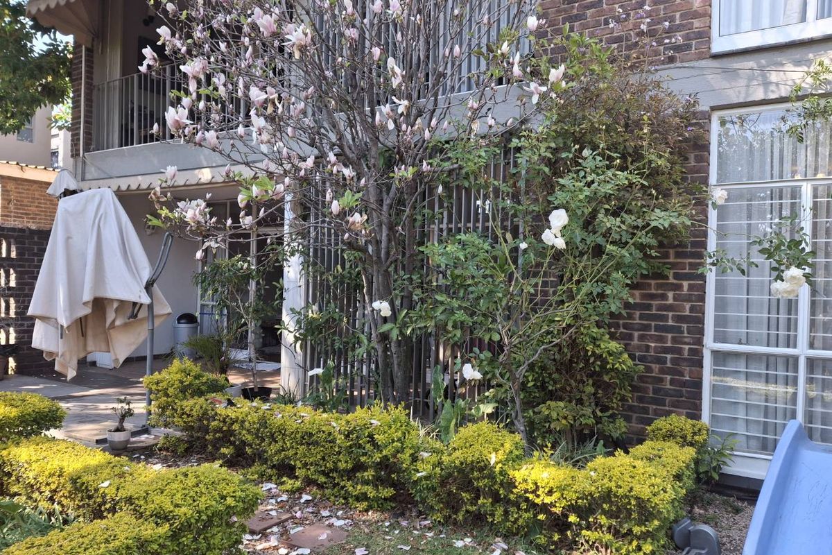 Rear view of the apartment featuring a brick facade, a private balcony, and a landscaped garden area with a paved patio.