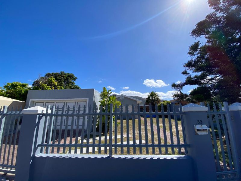 Front view of the property featuring a metal perimeter fence, brick driveway, and garage entrance under a clear blue sky.