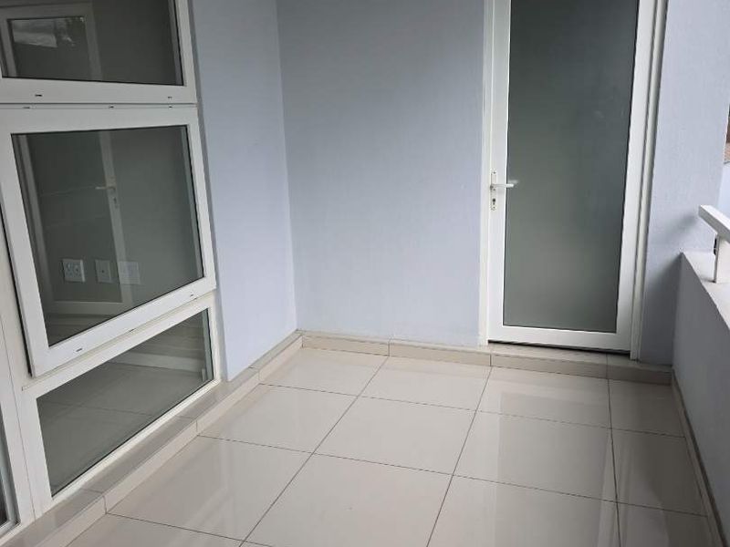 A clean, empty balcony featuring light-colored floor tiles, frosted glass door, and modern aluminium window frames, offering a bright and neutral outdoor space.
