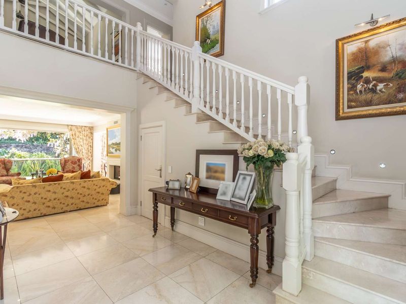 Elegant double-volume entrance hall featuring a grand marble staircase with white timber balustrades and polished stone flooring, leading into an open-plan living area.