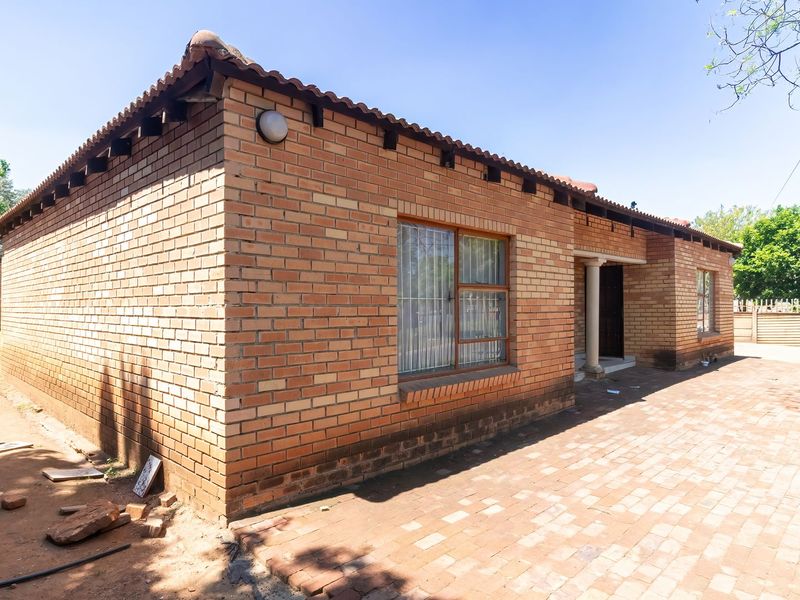 Rear view of a face brick house featuring a paved patio area, tiled roof, and security bars on the windows.
