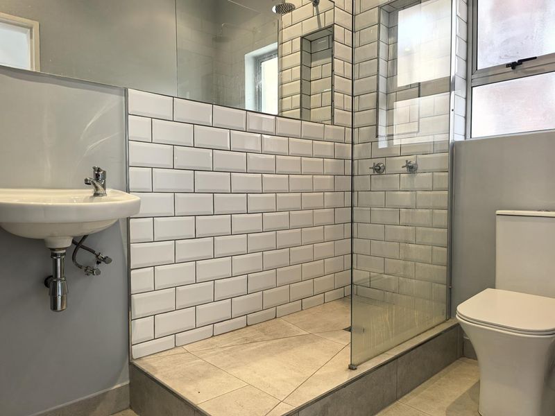 Modern bathroom featuring a walk-in shower with subway tile surround, glass screen, wall-mounted basin, and a standard toilet.