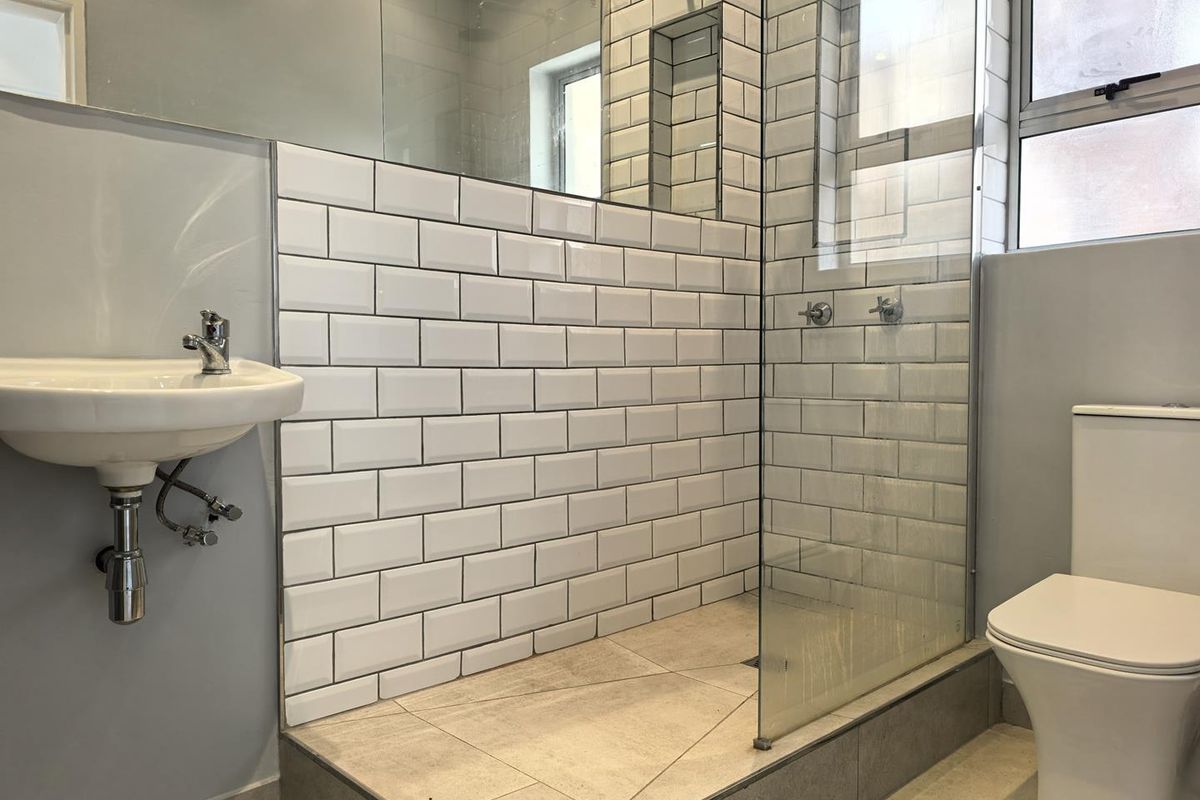 Modern bathroom featuring a walk-in shower with subway tile surround, glass screen, wall-mounted basin, and a standard toilet.