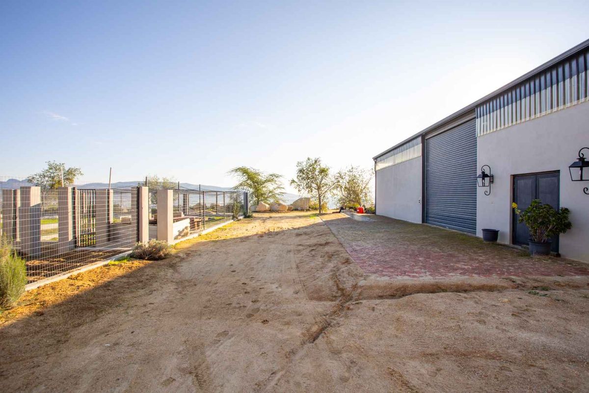 Rear exterior view of a farm building featuring a large roller shutter door, brick paved area, and mesh perimeter fencing.