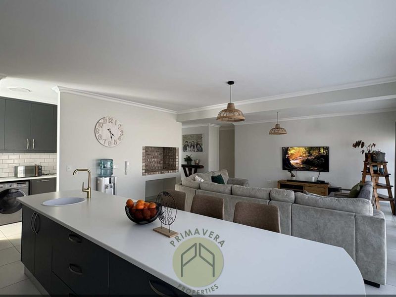 Spacious open-plan living area featuring a modern kitchen with a central island, tiled floors, and a cozy brick fireplace, perfect for family living.