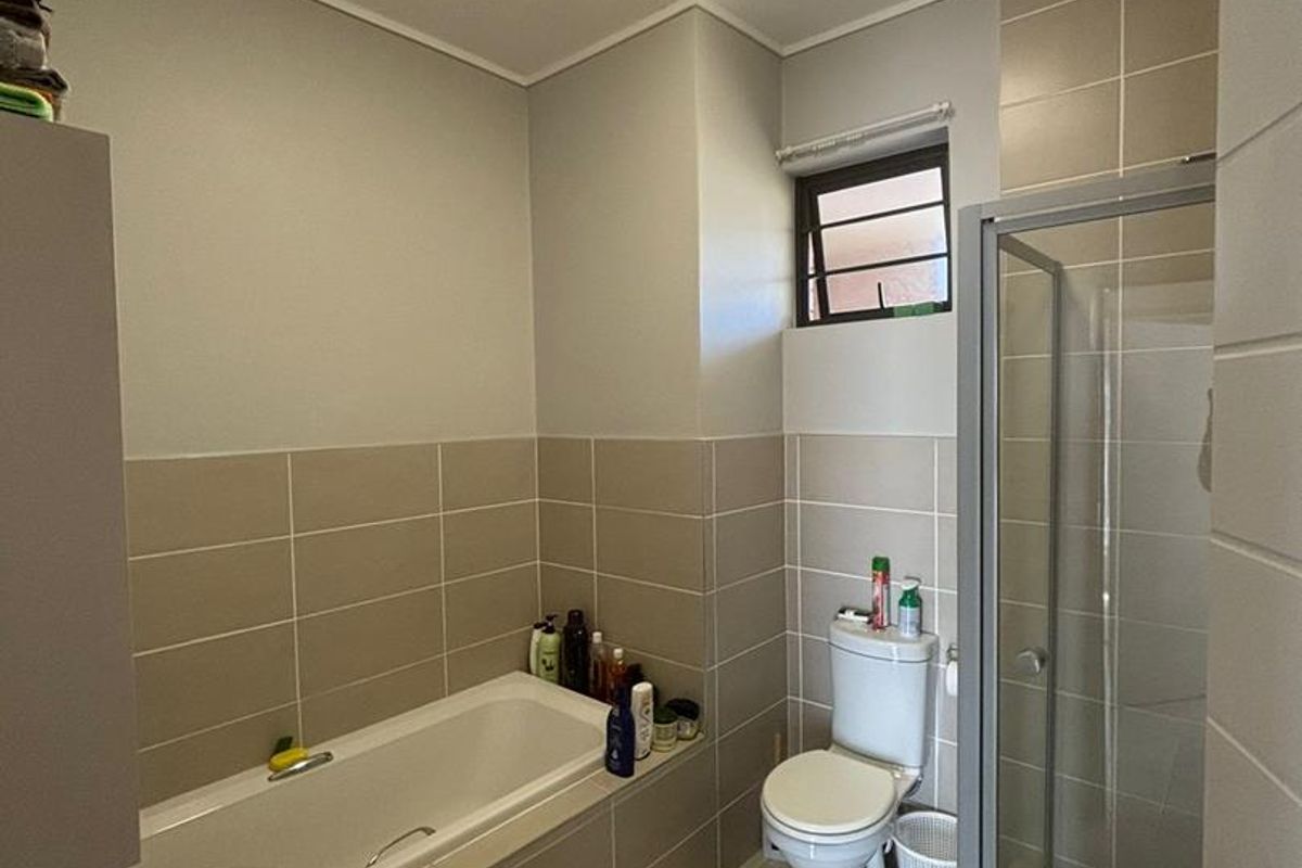 A functional bathroom featuring a built-in bathtub, a separate glass-enclosed shower, a toilet, and a wall-mounted basin with neutral wall tiling.