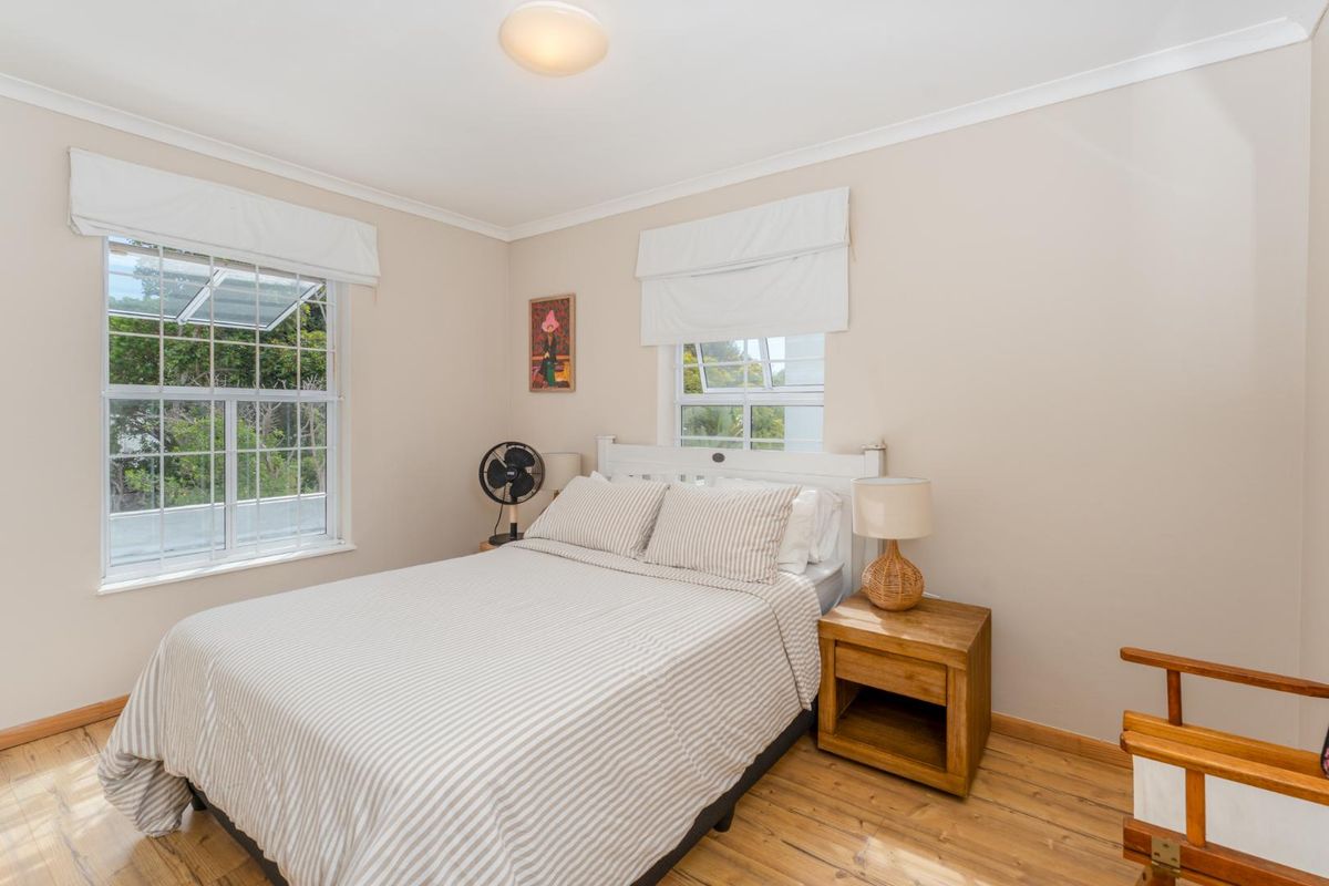 A bright and well-maintained bedroom featuring timber flooring, dual windows with fitted blinds, and neutral wall finishes.