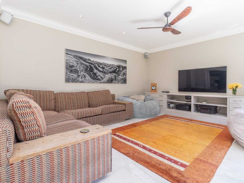 A comfortable living room featuring tiled flooring, recessed downlights, a ceiling fan, and custom built-in media cabinetry.