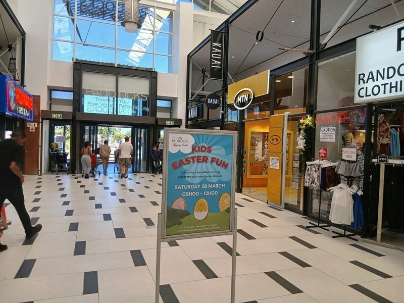 Interior view of a modern shopping centre concourse featuring glass storefronts, high ceilings with natural light, and tiled flooring.