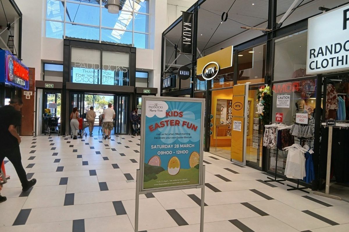 Interior view of a modern shopping centre concourse featuring glass storefronts, high ceilings with natural light, and tiled flooring.