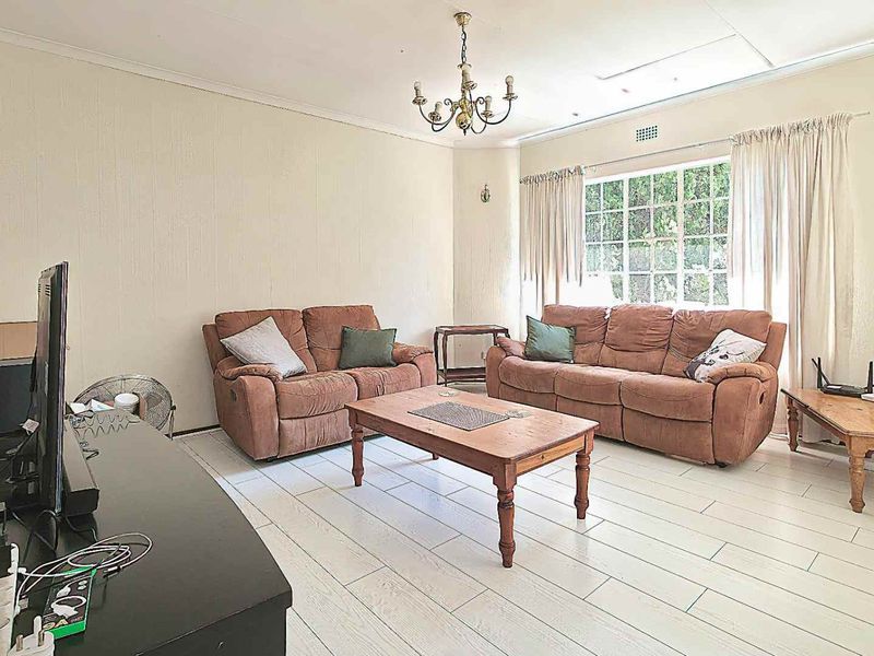 A spacious living room featuring light-colored tiled flooring, coving, and a large window that allows for natural light.