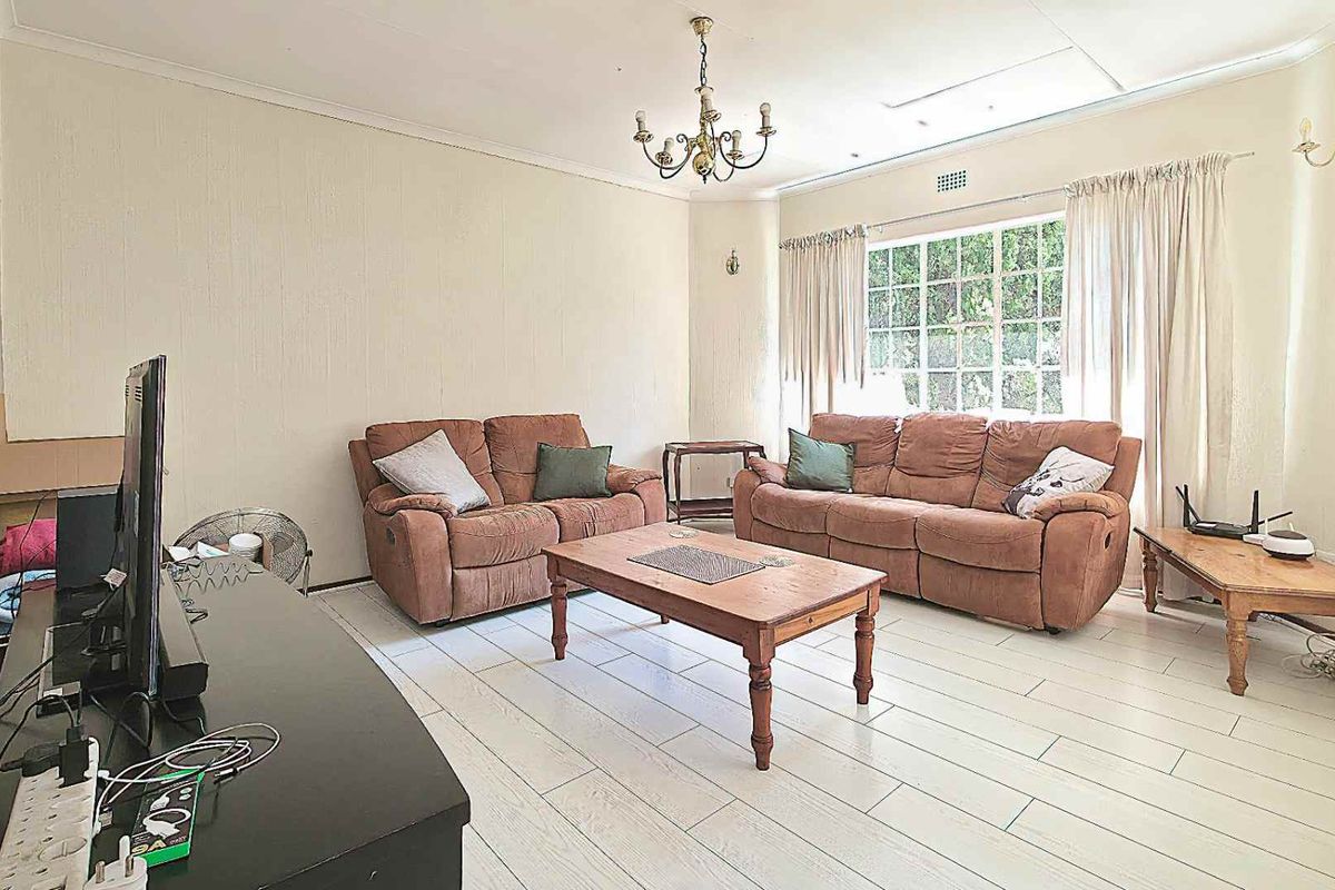 A spacious living room featuring light-colored tiled flooring, coving, and a large window that allows for natural light.