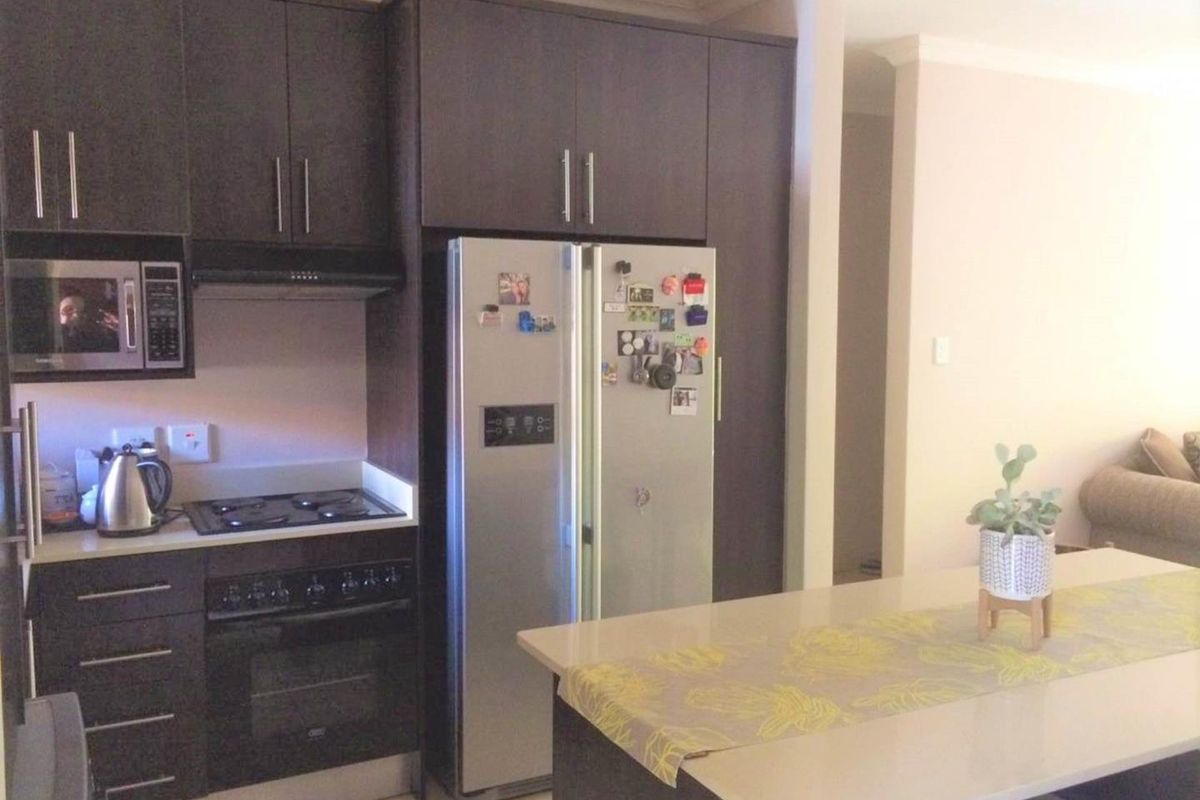 Modern kitchen featuring dark wood cabinetry, stone countertops, a central island, and integrated appliances including a built-in oven, hob, and microwave.