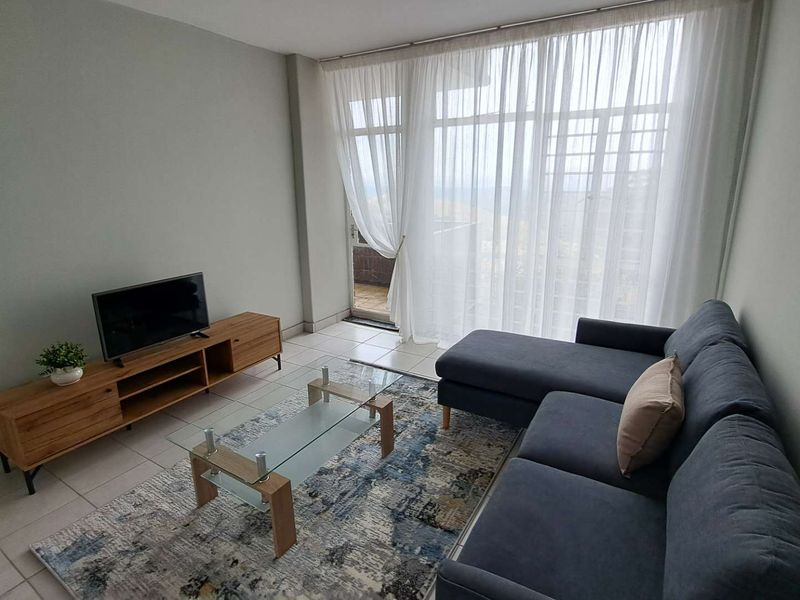 A bright living room featuring tiled flooring and a large sliding glass door with sheer curtains, providing access to an outdoor area.