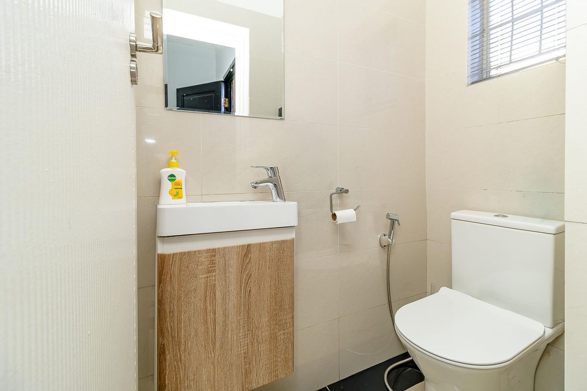 A compact guest bathroom featuring a modern wall-mounted vanity, basin, toilet, and bidet spray with neutral wall tiling.