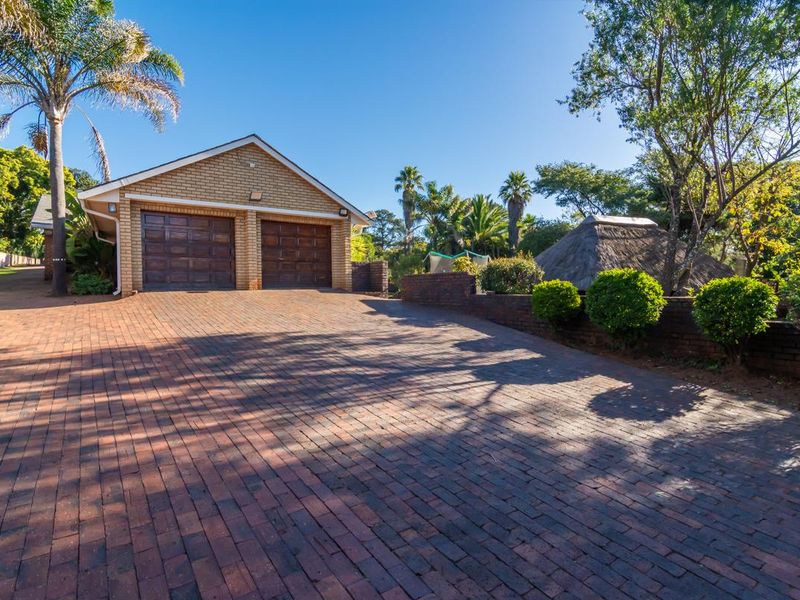 A spacious paved driveway leading to a double garage with brick facade and a well-maintained garden area.
