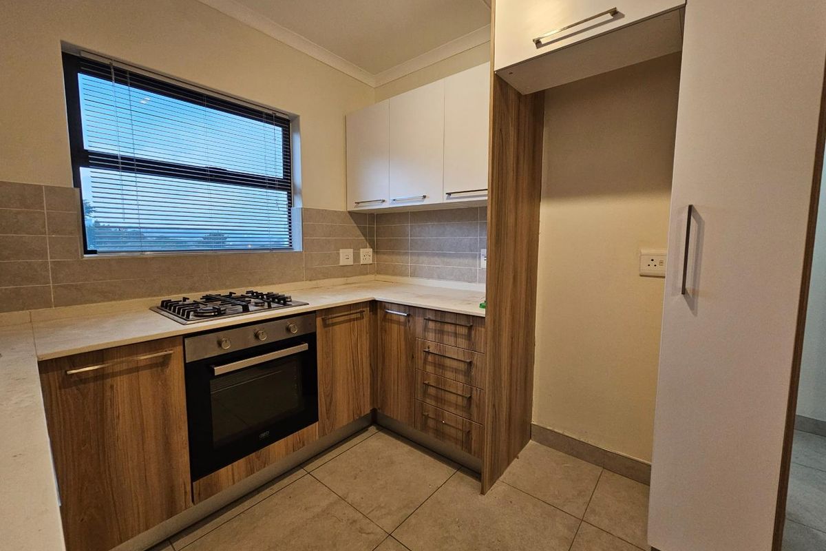 Modern kitchen featuring wood-grain cabinetry, stone-look countertops, a built-in oven, gas hob, and tiled flooring with a dedicated space for a refrigerator.