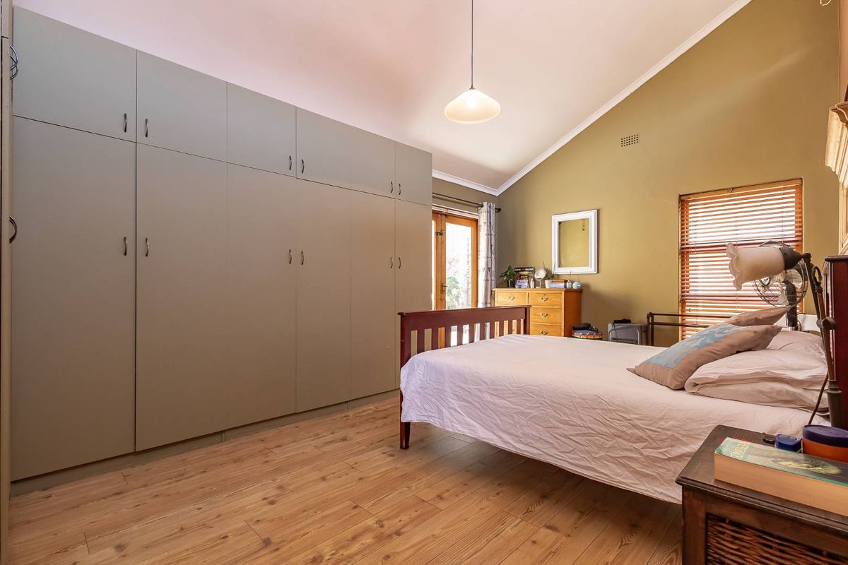 Spacious bedroom featuring high vaulted ceilings, wood-look flooring, and extensive floor-to-ceiling built-in cabinetry with direct access to an outdoor area.