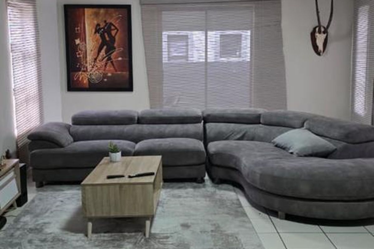 A spacious living room featuring neutral tiled flooring, multiple windows with fitted blinds, and modern flush-mount ceiling lighting.