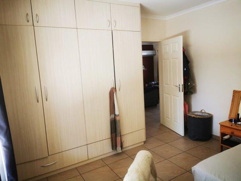 A bedroom featuring light wood-finish built-in cupboards and tiled flooring, with an open doorway leading to an adjacent room.