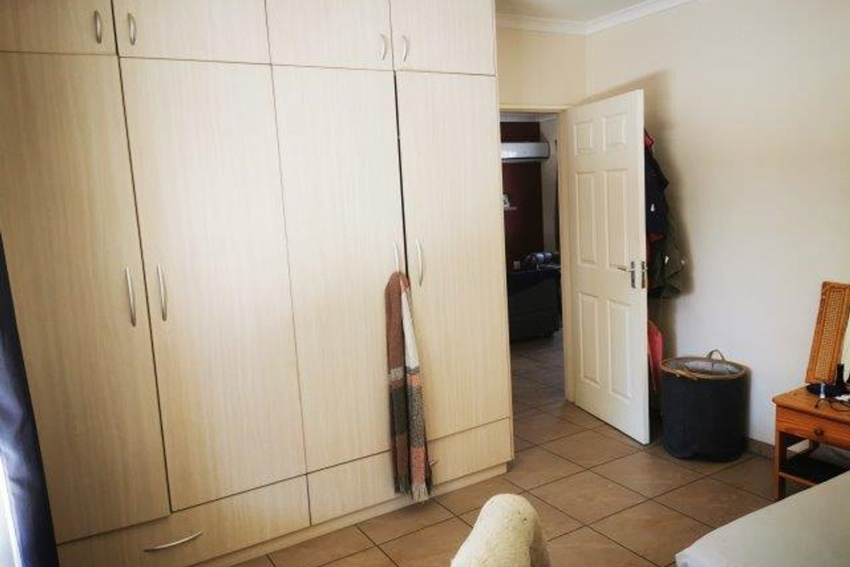 A bedroom featuring light wood-finish built-in cupboards and tiled flooring, with an open doorway leading to an adjacent room.