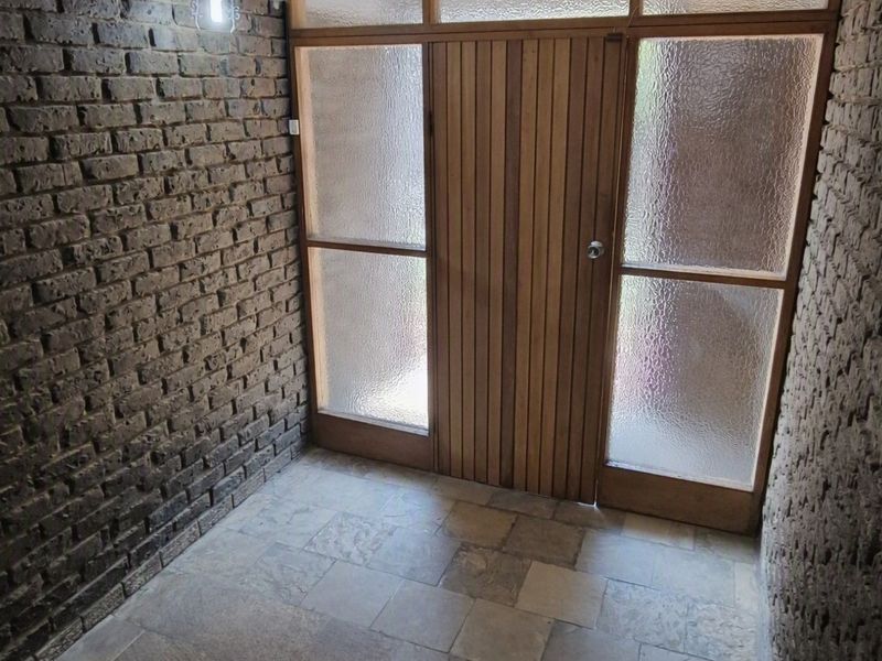 An entrance foyer featuring exposed brick walls, tiled flooring, and a timber-framed glass door providing natural light.