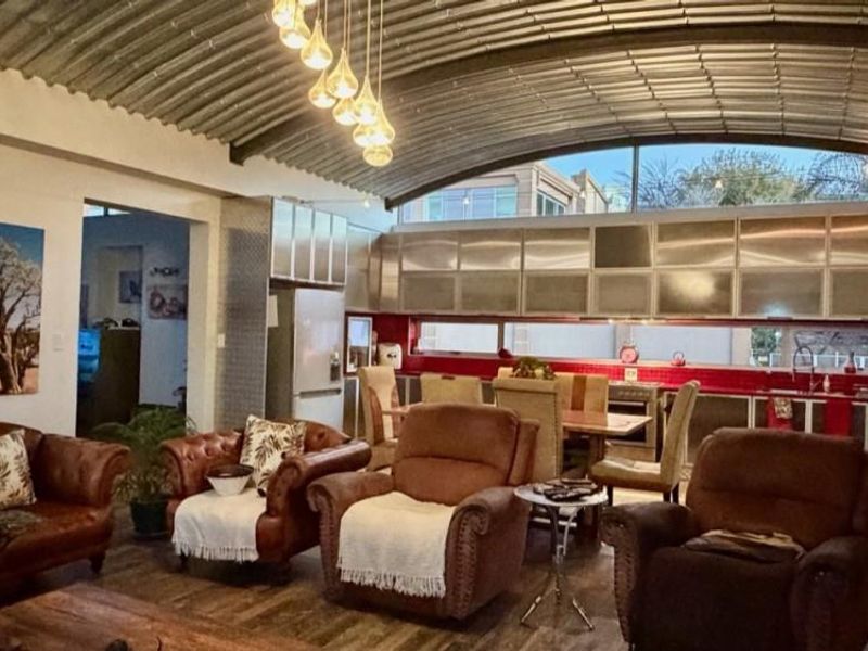 Spacious open-plan living and kitchen area featuring a distinctive corrugated metal barrel vault ceiling, modern stainless steel cabinetry, and a vibrant red tiled backsplash.