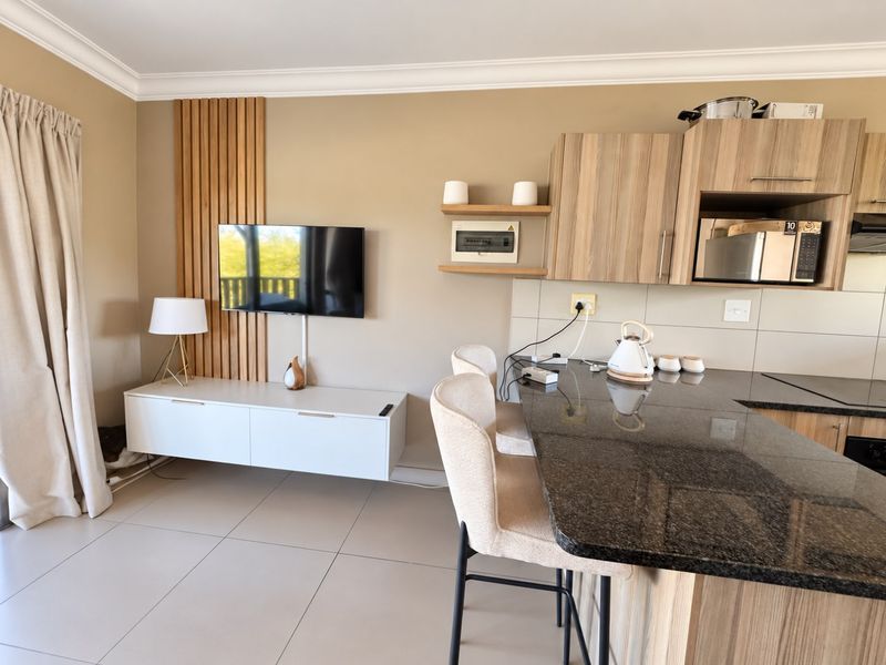 Modern open-plan living and kitchen area featuring granite countertops, timber slat wall detailing, and neutral tiled flooring in a well-maintained apartment setting.