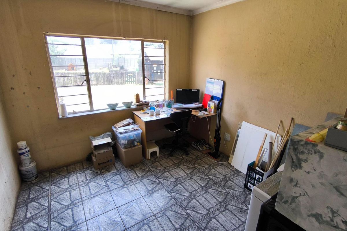 A small room featuring tiled flooring and a large window, currently utilized as a home office space.