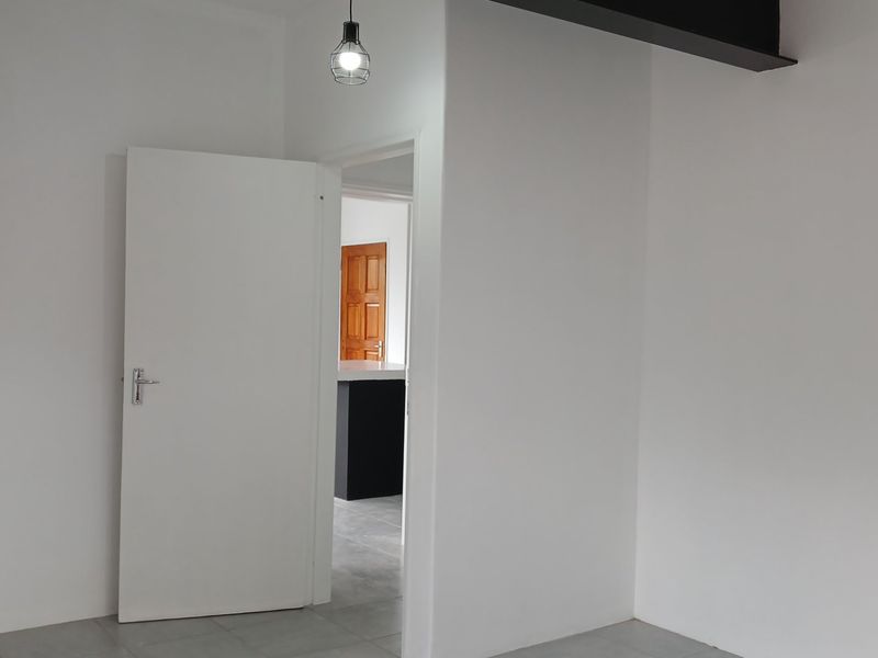 A clean, empty bedroom featuring neutral tiled flooring, a built-in cupboard, and a modern pendant light fixture.