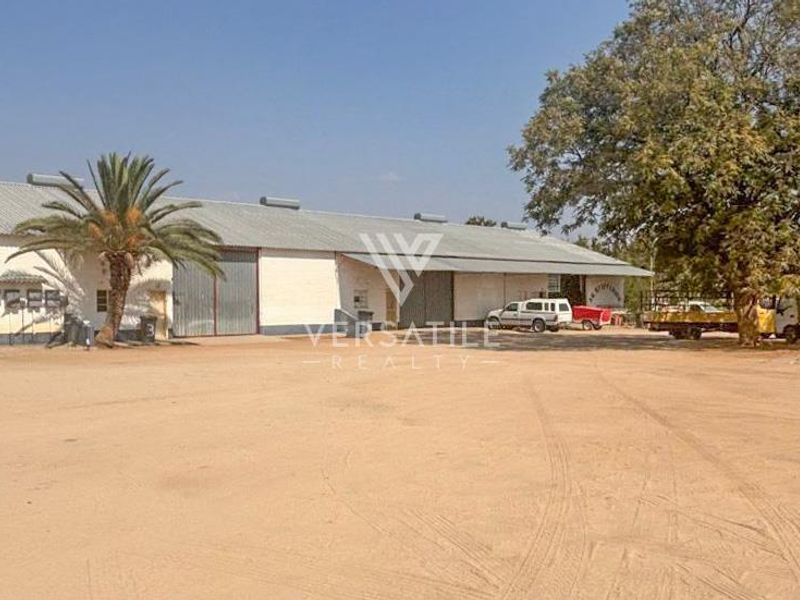 Industrial warehouse facility featuring large sliding access doors, corrugated metal roofing, and a spacious unpaved yard area for vehicle access.