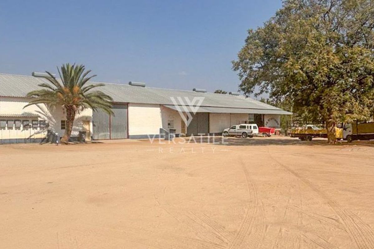 Industrial warehouse facility featuring large sliding access doors, corrugated metal roofing, and a spacious unpaved yard area for vehicle access.