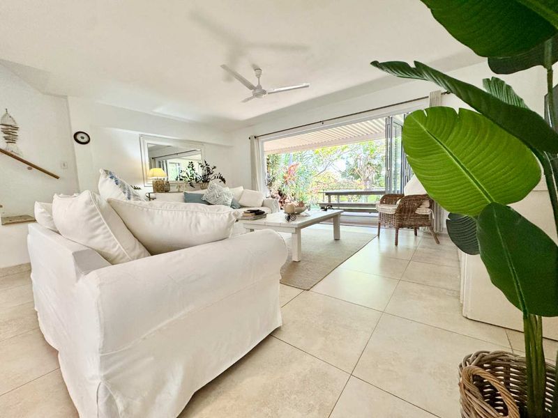 Bright and airy living room featuring large bi-fold doors that open onto a patio, complemented by neutral tiled flooring and a ceiling fan.