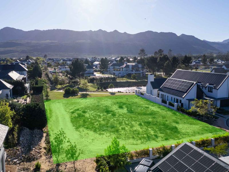 An aerial view of a vacant residential plot in a developed estate, highlighting the buildable area with mountain views.