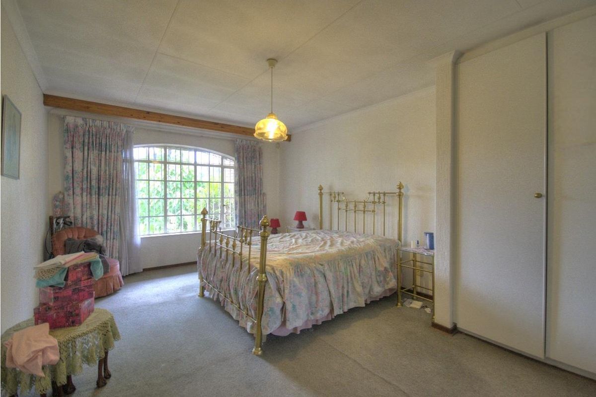 Spacious bedroom featuring built-in wardrobes, large arched window with security bars, and neutral wall finishes, offering a comfortable and functional living space.