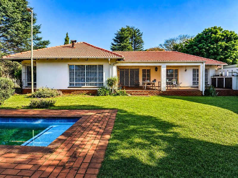 Rear view of the house featuring a well-maintained garden, a swimming pool with brick paving, and a covered patio area.