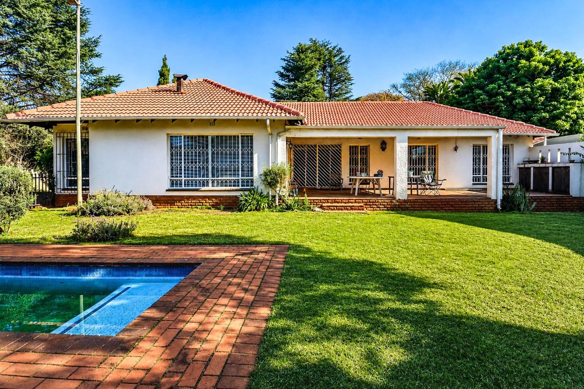 Rear view of the house featuring a well-maintained garden, a swimming pool with brick paving, and a covered patio area.